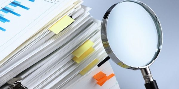 A stack of documents with labels, next to them is a magnifying glass.