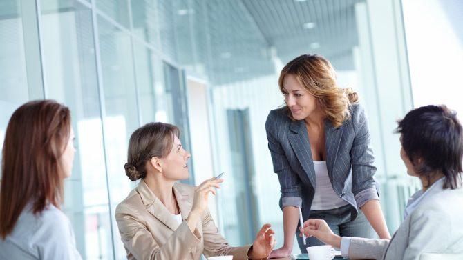 A group of four female coworkers is discussing something at a table.