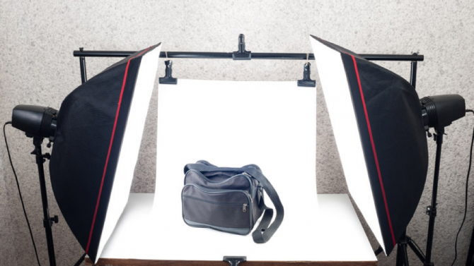 Eine lederne Tasche steht gut ausgeleuchtet zwischen zwei Fotoscheinwerfern und vor einem weißen Fotohintergrund.