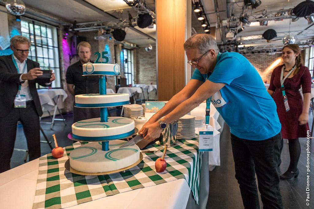 Picture of a man cutting a cake, while other persons look on and take pictures.