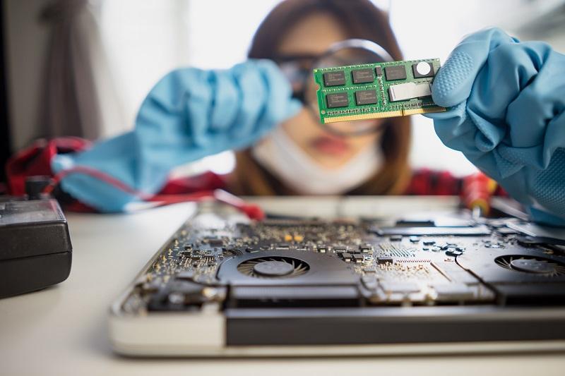 A female computer technician is inspecting a printed circuit board with some processor chips with the help of a magnifying glass.