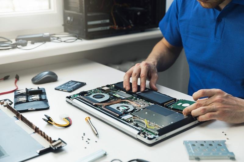 A man is adjusting the hardware components of a partially disassembled laptop on a table in front of him.