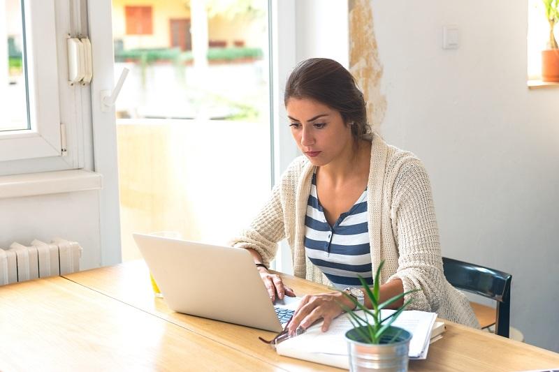 Eine Frau sitzt an einem Tisch und arbeitet mit einem Laptop.