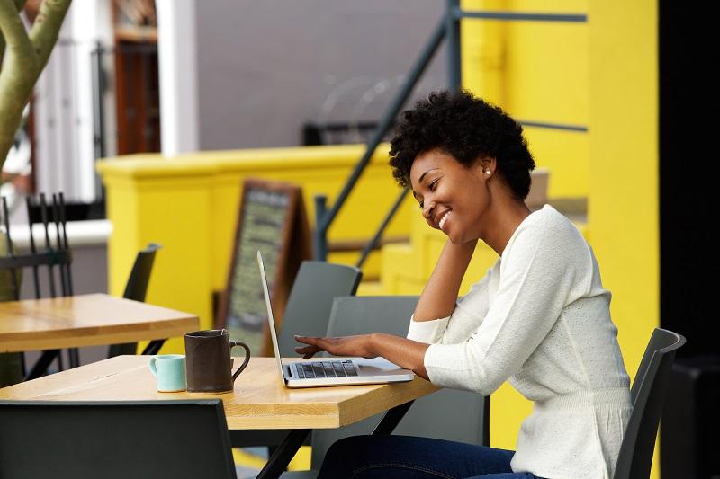 A young woman is smiling and working on her laptop.