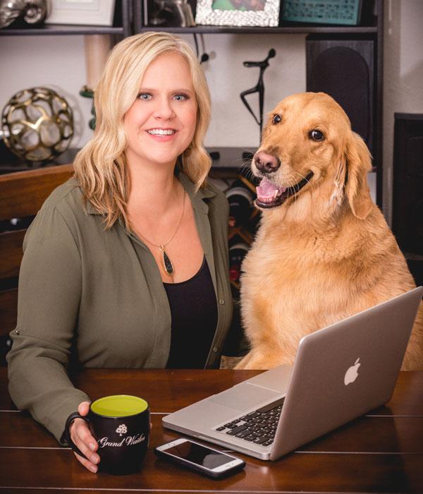 Carin Martens sitting at a table with a laptop and a large dog next to her.