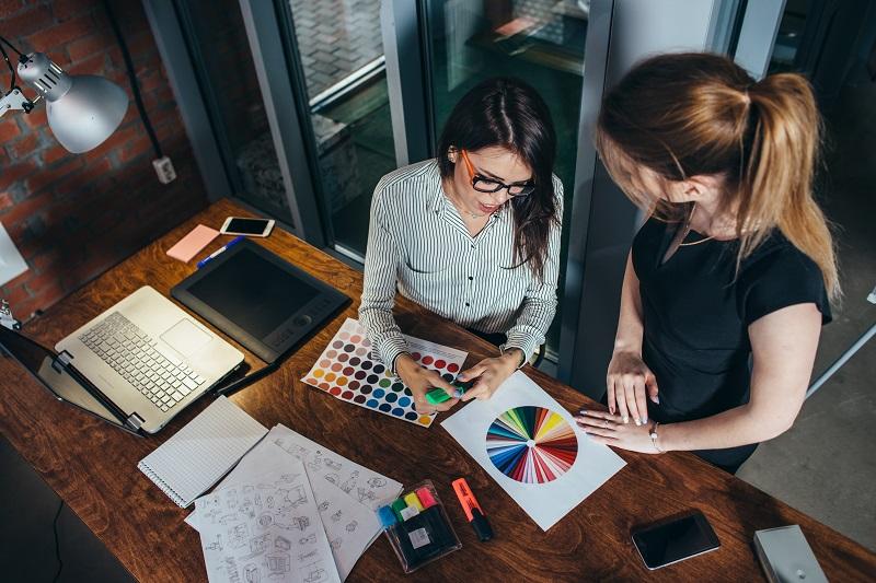 Two female workers going over graphic designs next to a laptop.