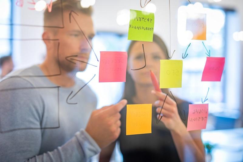 A man and woman in an office review a board of notes.