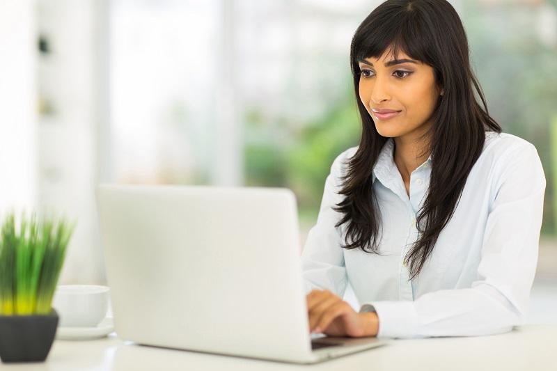 Eine junge Frau arbeitet an ihrem Schreibtisch sitzend mit ihrem Laptop.