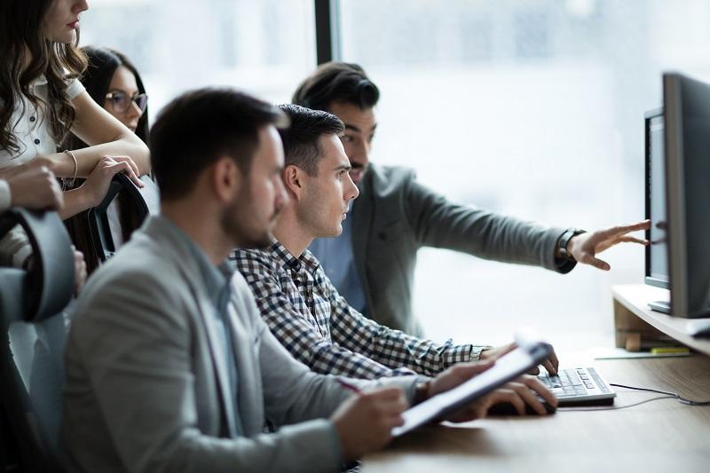 Mehrere junge Kollegen in einem Büro betrachten gemeinsam einen Computerbildschirm.