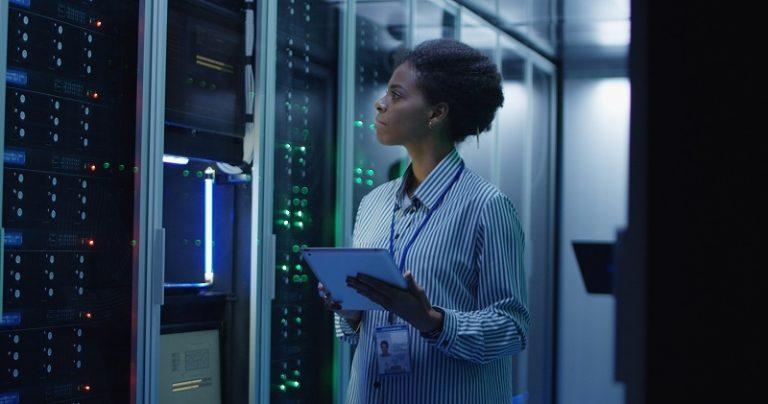 Eine Frau steht in einem modernen Serverraum und überprüft die Computerserver.