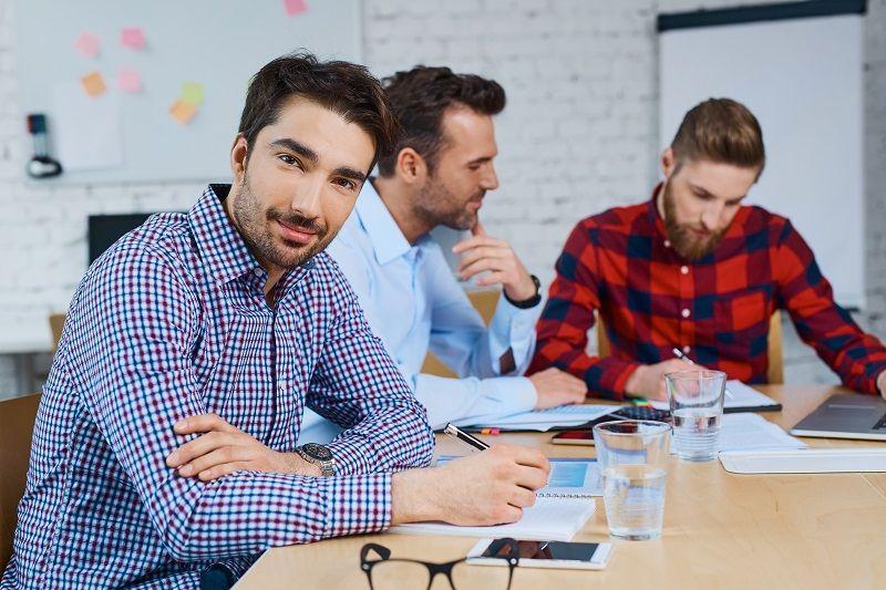 Drei junge Männer sitzen gemeinsam an einem Bürotisch und arbeiten zusammen.