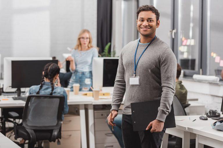 Ein Mann in einem Büro lächelt in die Kamera, während im Hintergrund ein Team an der Wiederherstellung der Markenreputation arbeitet.
