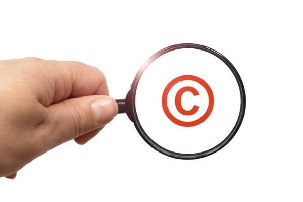 Eine Hand mit einem Vergrößerungsglas, das ein Copyright-Zeichen vergrößert.