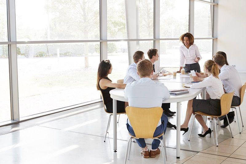 An einem Tisch sitzt eine Gruppe Arbeiter in einheitlicher Kleidung in einer Besprechung und lauscht den Ausführungen ihres Vorgesetzten zum Thema Teamarbeit-Strategien.