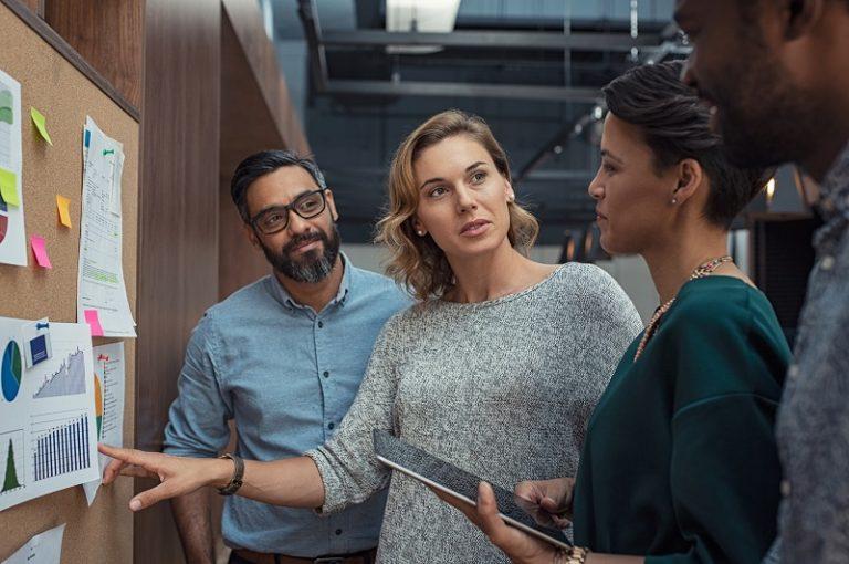 Eine Gruppe von Mitarbeitern diskutiert vor einer Pinnwand über das Thema Enterprise Content Management.