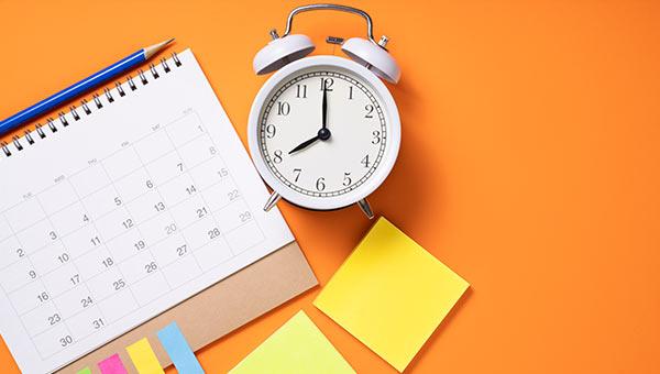 An alarm clock on a desk with a calendar.