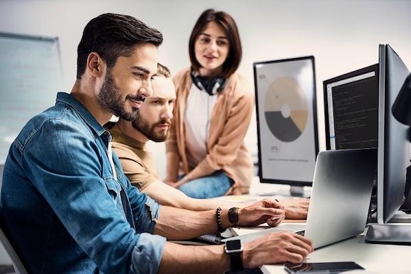 Zwei männliche Kollegen und eine weibliche Kollegin arbeiten mit verschiedenen Computern an der Erstellung von Grafiken.