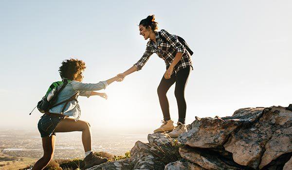 One person helping another up a cliff.