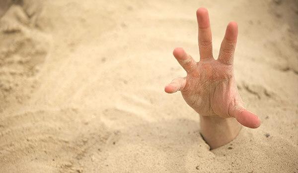 A hand being buried in sand.