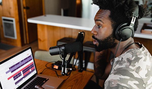 Ein junger Mann zeichnet mit seinem Laptop einen Podcast auf.