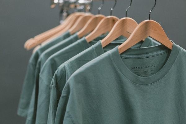 Five identical green T-shirts hanging on a display rack.