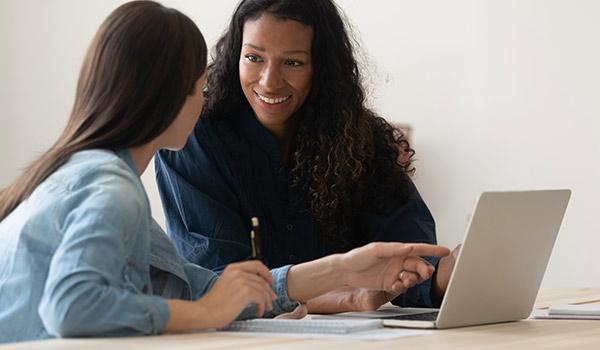 Two women sitting at a computer discussing an email draft.