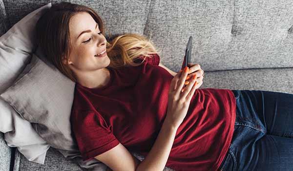 Woman in red shirt lying on a sofa watching a video on her phone.