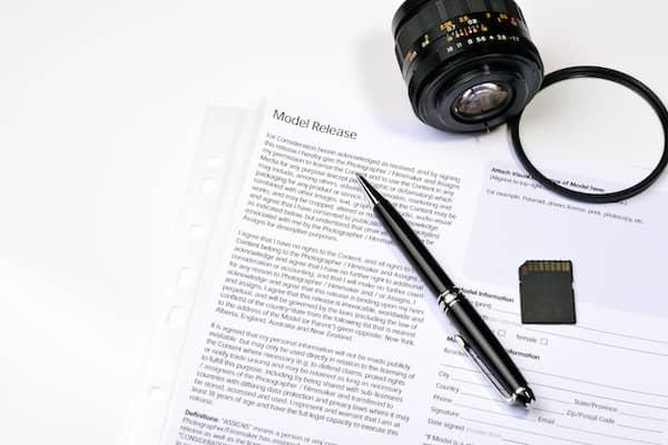 Neben einem Kameraobjektiv liegen eine Speicherkarte, ein Stift und eine Einverständniserklärung mit der Überschrift Model Release.