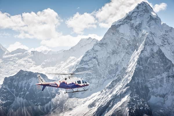 A helicopter flies past a snow-covered mountain range.