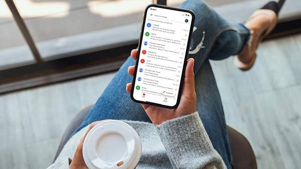 Eine Frau hält ein Smartphone, auf dessen Bildschirm das E-Mail-Postfach angezeigt wird.