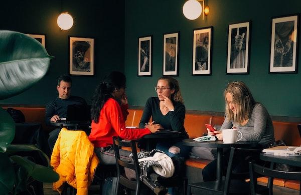 Kunden sitzen in einem modernen Café, hinter ihnen hängen Schwarz-Weiß-Fotos an der Wand.