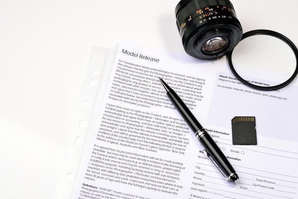 Neben einem Kameraobjektiv liegen eine Speicherkarte, ein Stift und eine Einverständniserklärung mit der Überschrift Model Release.