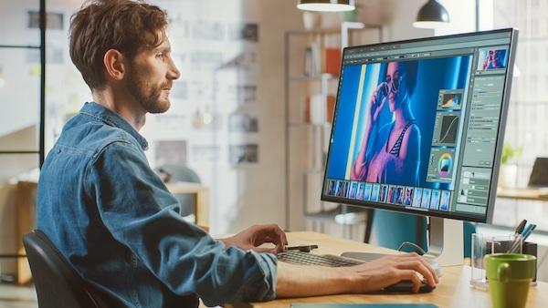 Ein Grafikdesigner sitzt am Schreibtisch und arbeitet an einem Computer, weil er JPG in PSD konvertieren möchte.