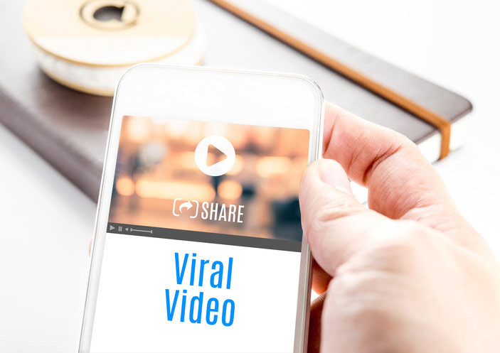 Eine Person hält ein Smartphone, auf dessen Bildschirm die Worte 'virales Video' stehen.