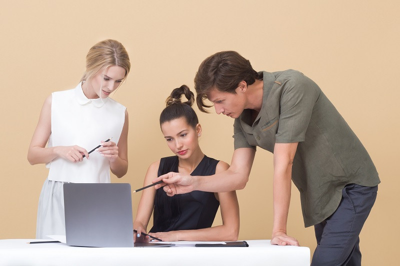 Drei Mitarbeiter stehen vor einem Laptop und beraten sich zum Thema Marketing-Projektmanagement.