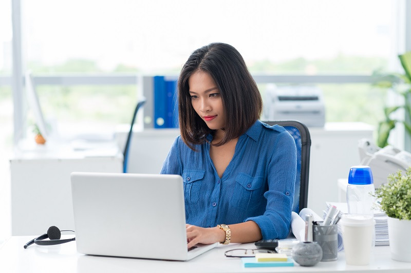 Eine junge Frau sitzt in einem modernen Büro an einem Schreibtisch und benutzt einen Laptop.
