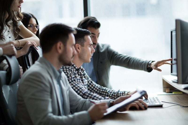 Mehrere junge Kollegen in einem Büro betrachten gemeinsam einen Computerbildschirm.