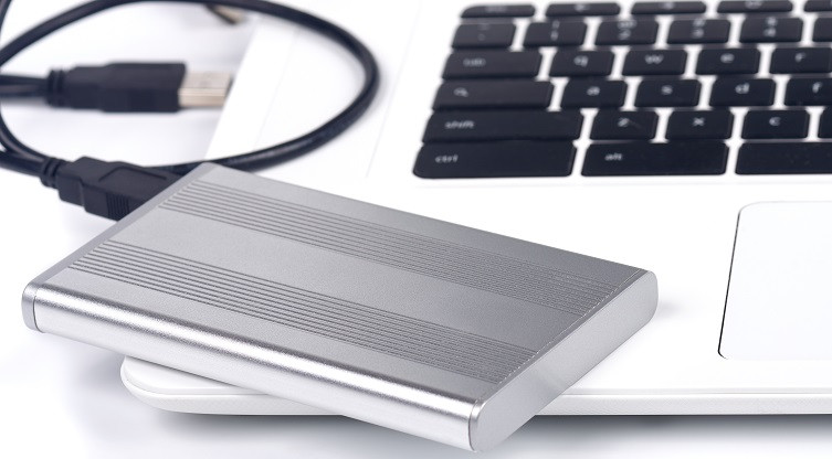Eine mobile Festplatte liegt neben der Tastatur eines Laptop.