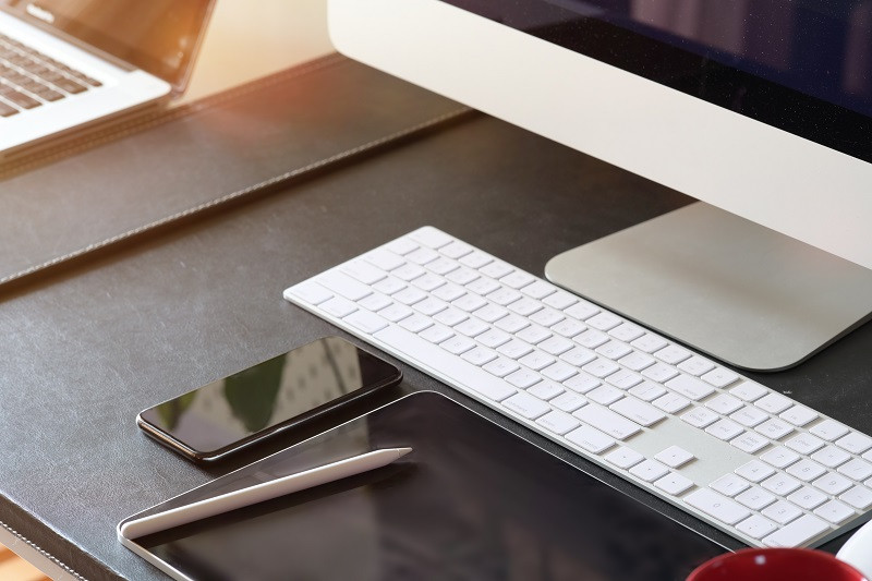 Ein Bild von einem Schreibtisch, auf dem sich ein Apple-Computer, ein Smartphone und ein Tablet-PC befinden.