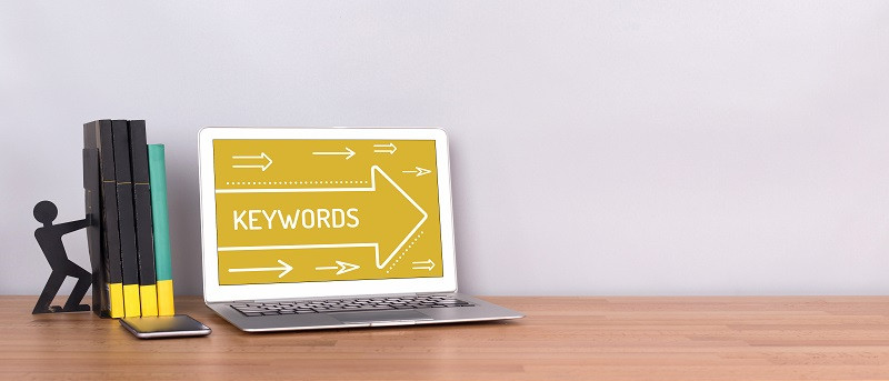 Ein Bild von Büchern neben einem Laptop, auf dem der Begriff 'Keywords' steht.