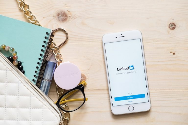 Ein Bild von einem Schreibtisch mit einem Mobiltelefon, auf dem die Seite von LinkedIn angezeigt wird.