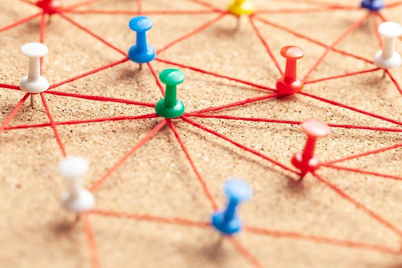 Eine Pinnwand mit Stecknadeln, die mit Fäden untereinander verbunden sind und ein Netzwerk symbolisieren.