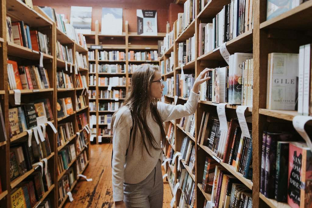 Eine junge Studentin betrachtet die Bücher in den vollen Regalen einer Bibliothek.