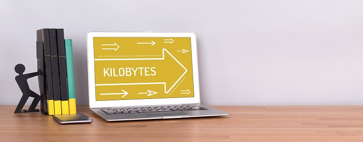 Ein Laptop steht auf einem Tisch neben einigen Büchern, auf seinem Bildschirm steht das Wort 'Kilobytes'.