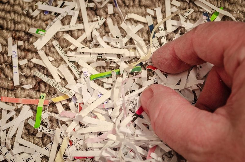 Eine Hand sammelt Schnipsel aus einem Haufen geschredderten Papiers.