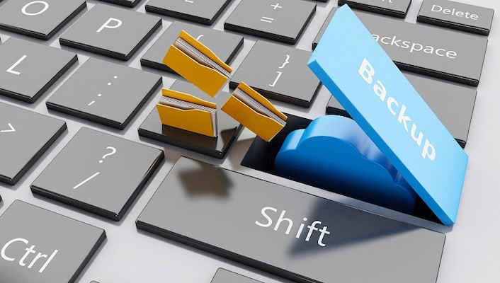 Eine Tastatur, auf der eine aufgeklappte Taste mit dem Wort Backup beschriftet ist, unter der sich ein Symbol für einen Cloud-Speicher verbirgt, auf das sich Dateisymbole zubewegen.