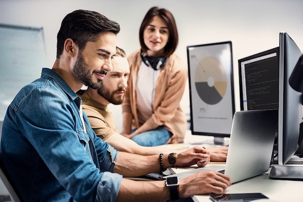 Zwei männliche Kollegen und eine weibliche Kollegin arbeiten mit verschiedenen Computern an der Erstellung von Grafiken.