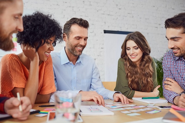 Ein Team in einem Büro sichtet Notizen zum Management für kreative Projekte auf einem Tisch.