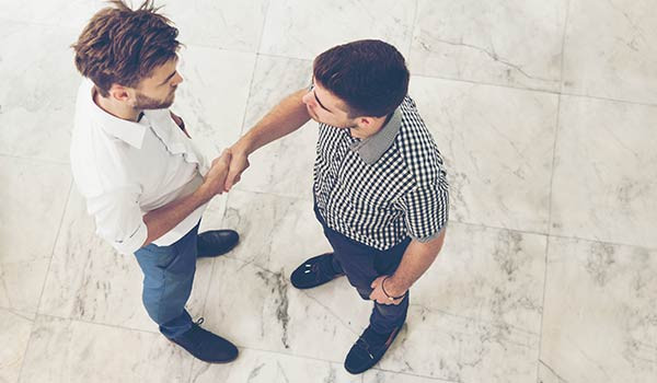 Zwei junge Männer schütteln sich die Hand, als Symbol dafür, dass Aufrichtigkeit ein Grundbaustein für Markenauthentizität ist.
