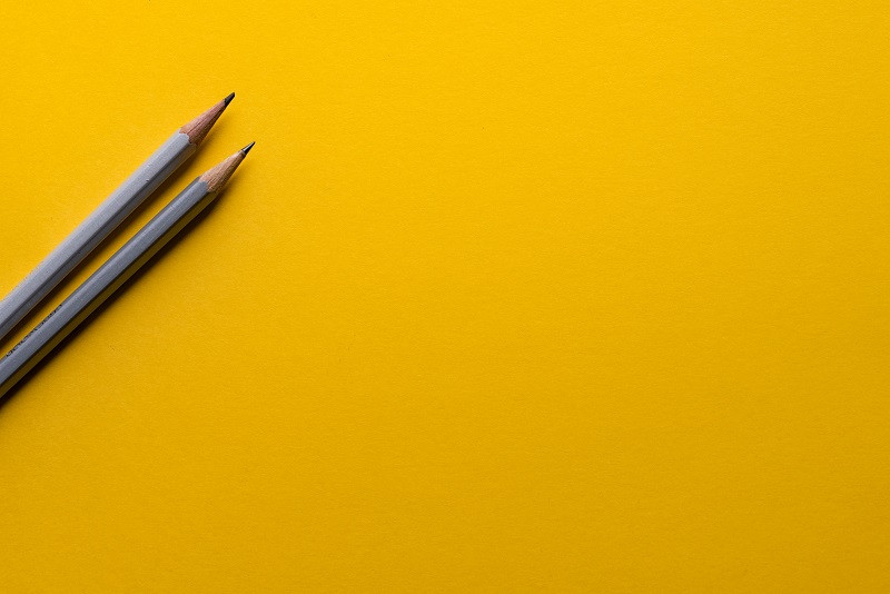 Ein gelber Hintergrund, auf dem zwei Bleistifte liegen.